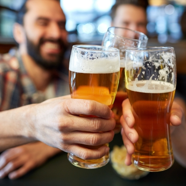 Three friends toast with beers, smiling and celebrating at a restaurant in Glyndon MN.