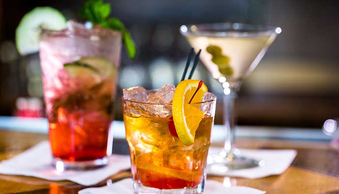 Three colorful cocktails at a Restaurant in Glyndon MN, garnished with fruit, olives, and mint.