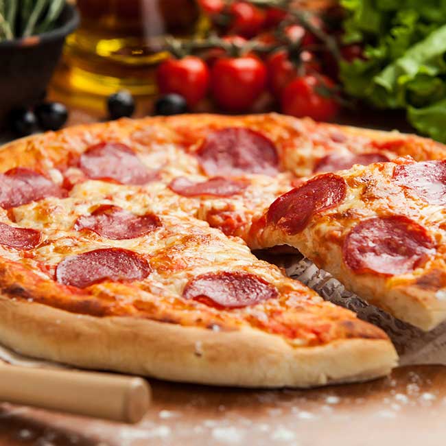 A pepperoni pizza with one slice lifted at a cozy restaurant in Glyndon MN, veggies behind.