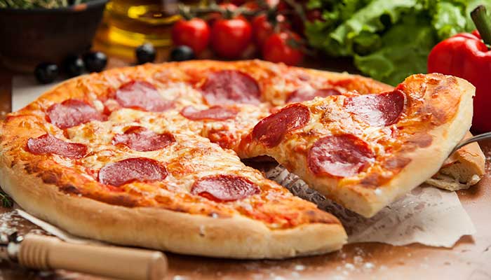 A slice of pepperoni pizza lifted, fresh at a restaurant in Glyndon MN, veggies in background.